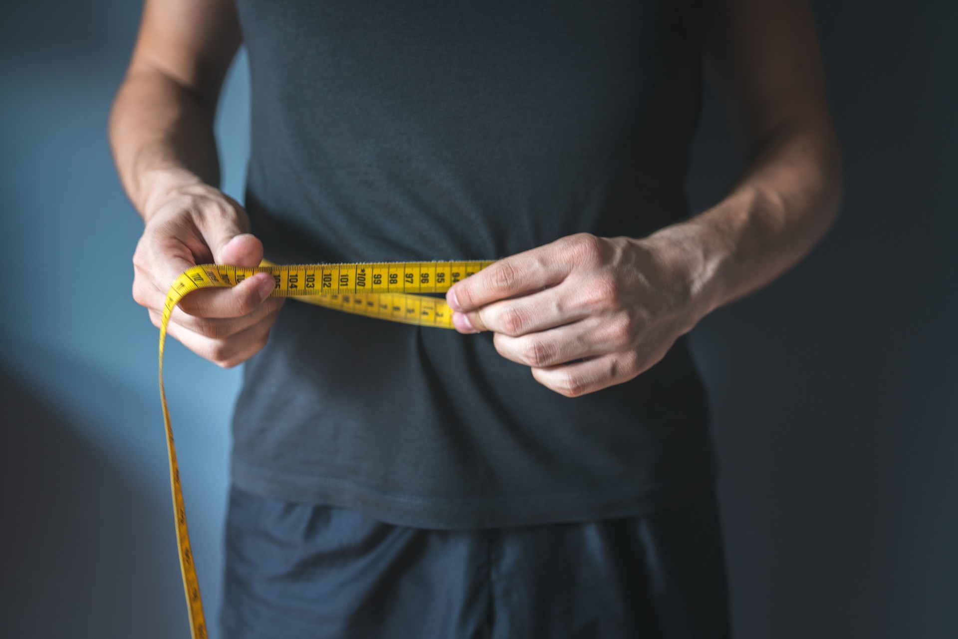 Slim man measuring his waist. Healthy lifestyle, body slimming, weight loss concept.